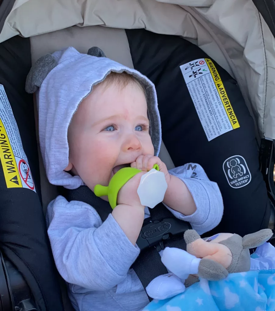 A baby in a car seat chewing on a toy