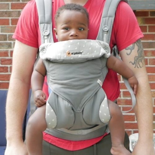 A baby in the Ergobaby 360 carrier being carried by a guy with a red shirt